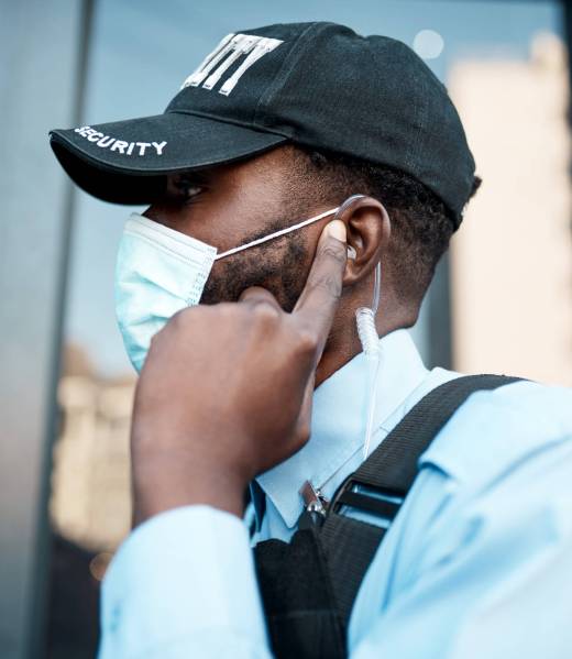 Shot of a masked young security guard using an earpiece while on patrol outdoors.